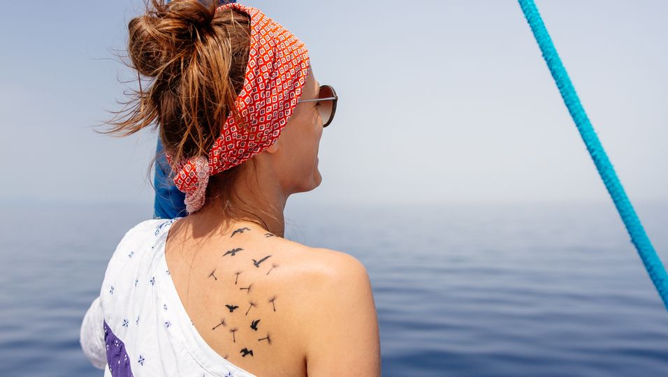 Frau mit Tattoo auf dem Rücken blickt aufs Meer