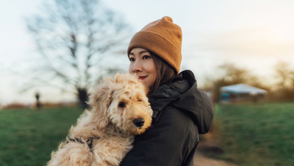 Frau hält Hund auf dem Arm und lächelt
