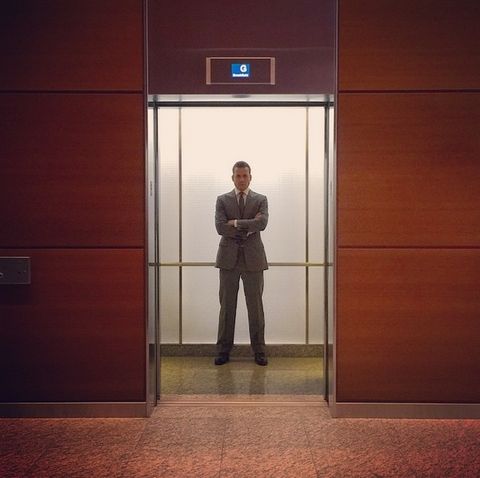 Patrick Adams steht im Anzug in einem Aufzug