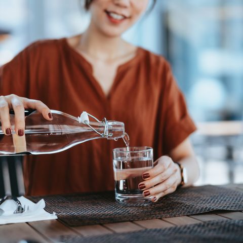 Frau schenkt Wasser aus einer Karaffe in ein Glas