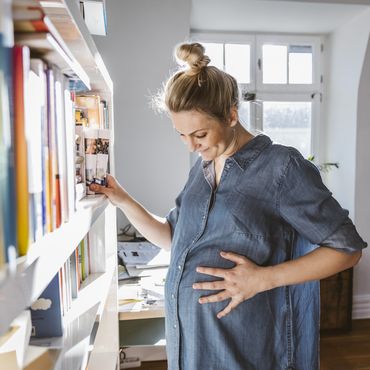 Schwangere Frau steht vor Bücherregal