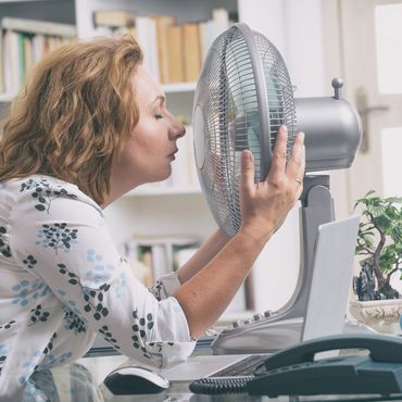 Frau kühlt ihr Gesicht vor einem Ventilator