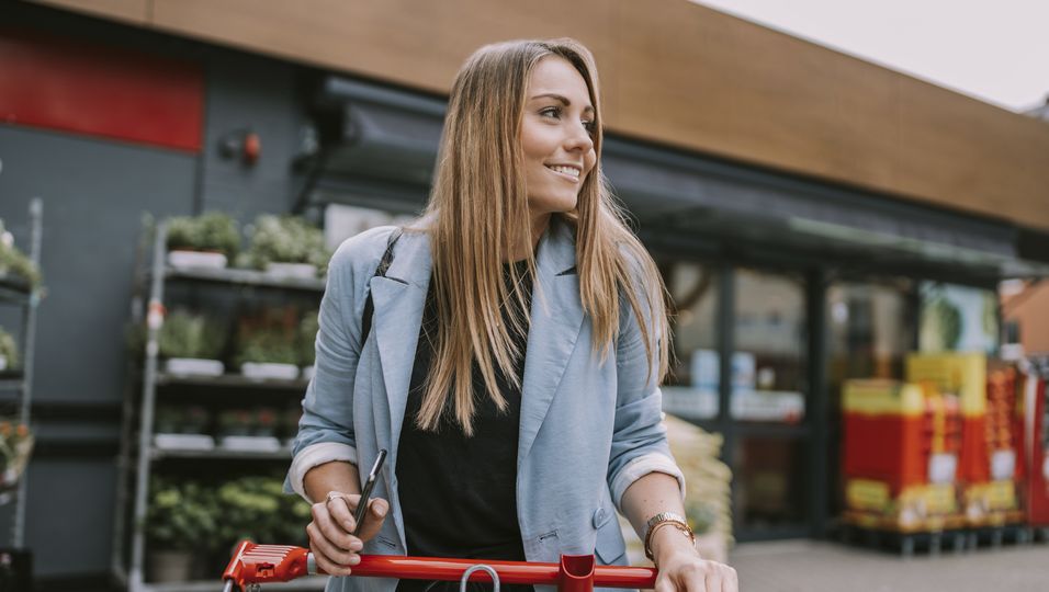 Frau auf einem Parkplatz von einem Supermarkt mit Einkaufswagen