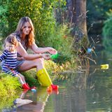 Frau in Gummistiefeln lässt mit ihrer Tochter Papierschiffchen schwimmen