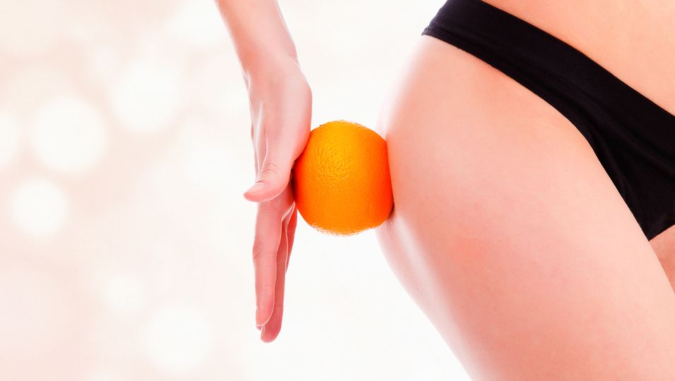 Frau hält Orange am Oberschenkel - Ausschnitt