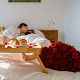 Paar liegt mit Frühstück und Rosen im Bett