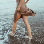 Frau im Sommerkleid läuft durchs Wasser