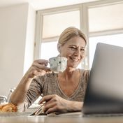 Frau trinkt Kaffee und schaut auf Laptop