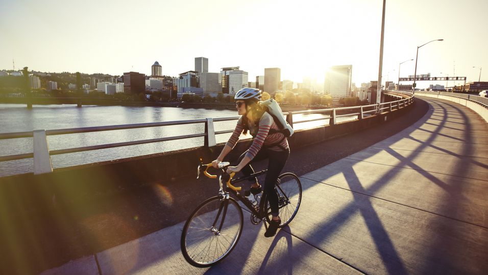 Frau fährt mit dem Fahrrad über eine Brücke in eienr Stadt