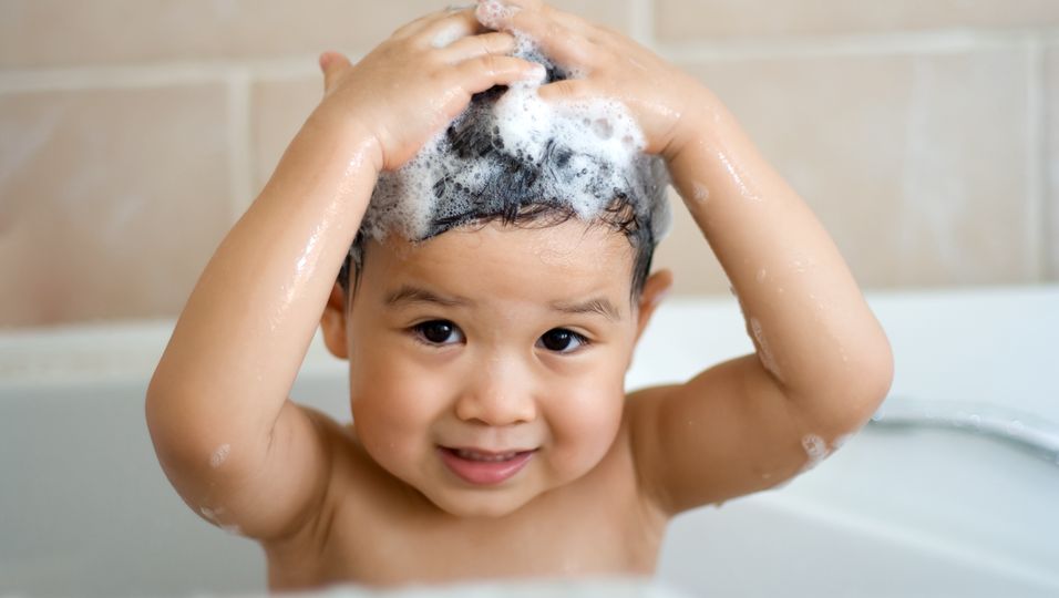 Baby sitzt in der Badewanne und hat Shampoo im Haar