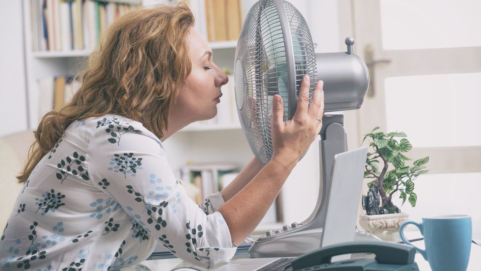 Frau kühlt ihr Gesicht vor einem Ventilator