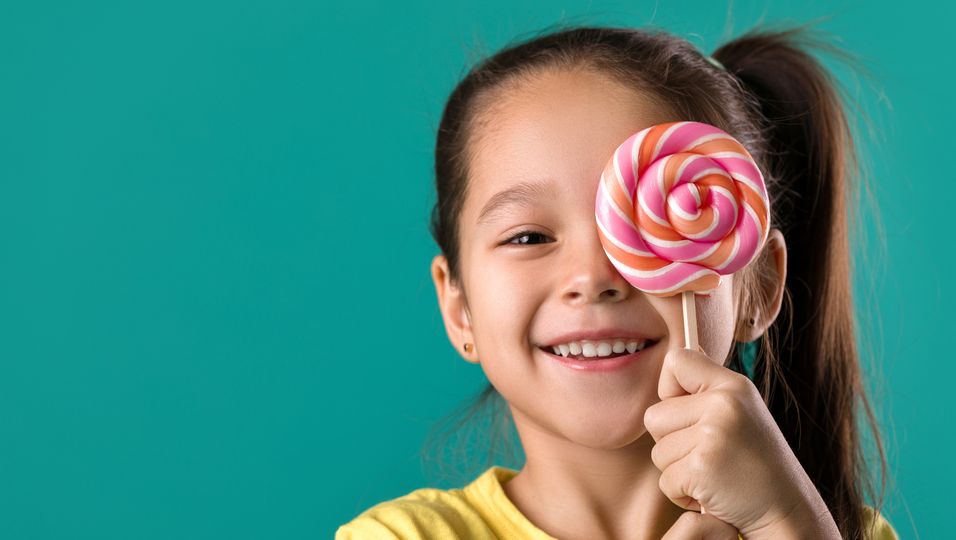 Kleines Mädchen, die sich einen Lollipop vor das Gesicht hält.