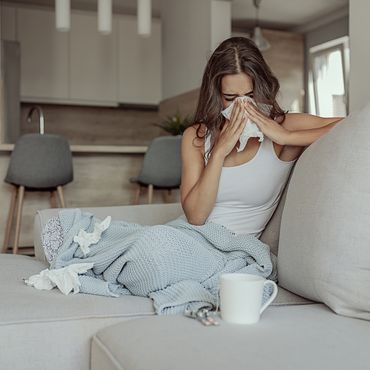 Erkältete Frau sitzt auf einem Sofa und putzt sich die Nase
