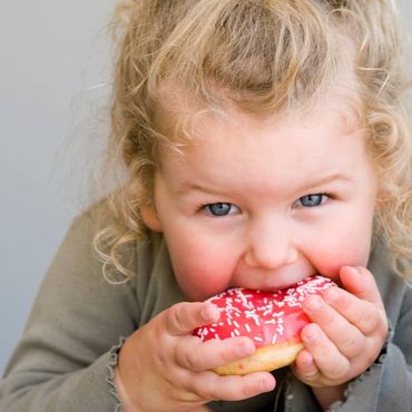 Little girl eating jelly-glazed donut with sprinkles