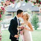 Küssendes Brautpaar unter Blumenbogen