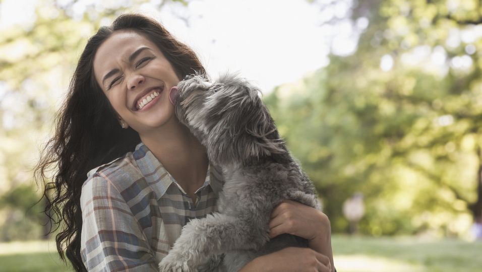 Frau hält Hund auf dem Arm, der sie an der Wange abschleckt