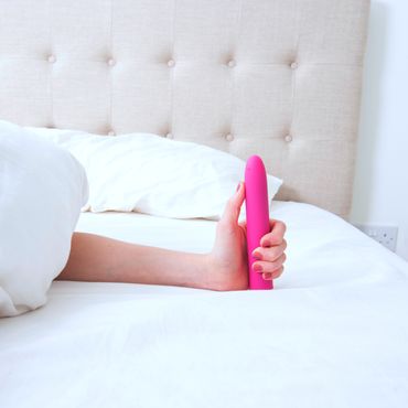 Eine Frau, die im Bett liegt und einen Vibrator in der Hand hält.