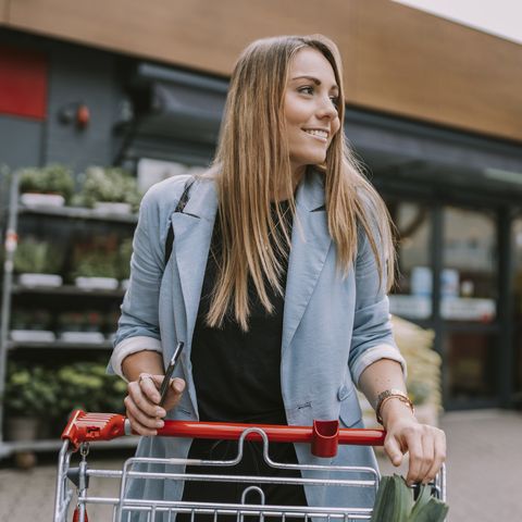 Frau auf einem Parkplatz von einem Supermarkt mit Einkaufswagen
