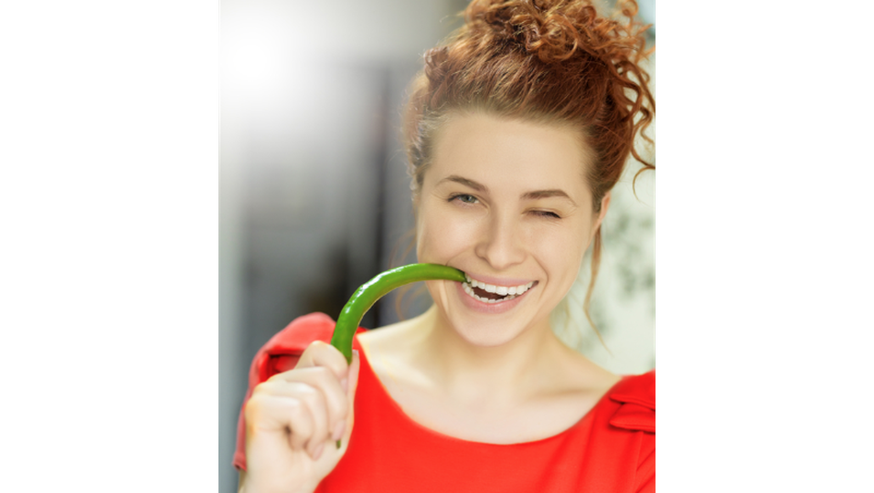 Junge Frau beißt auf eine grüne Chili-Schote